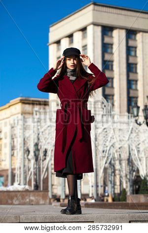 Full body portrait. Young beautiful brunette woman in stylish in a long burgundy coat walking in spring street