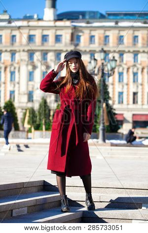 Full body portrait. Young beautiful brunette woman in stylish in a long burgundy coat walking in spring street