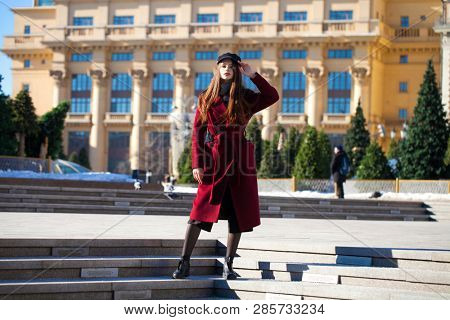 Full body portrait. Young beautiful brunette woman in stylish in a long burgundy coat walking in spring street