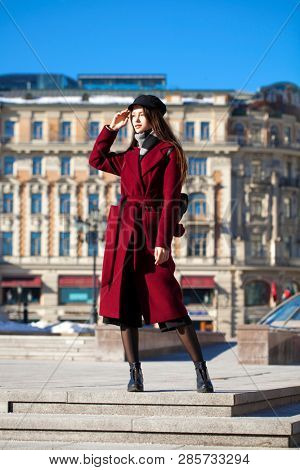 Full body portrait. Young beautiful brunette woman in stylish in a long burgundy coat walking in spring street