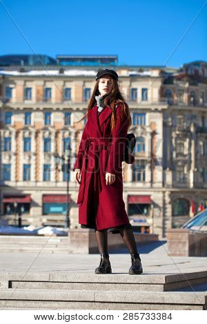 Full body portrait. Young beautiful brunette woman in stylish in a long burgundy coat walking in spring street