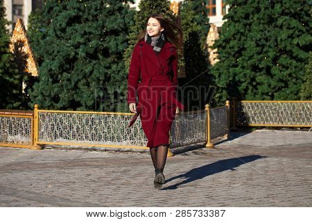Full body portrait. Young beautiful brunette woman in stylish in a long burgundy coat walking in spring street