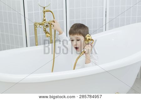 Baby In The Bathroom In Clothes.the Boy Sits In The Bath And Plays The Phone.talking On The Phone