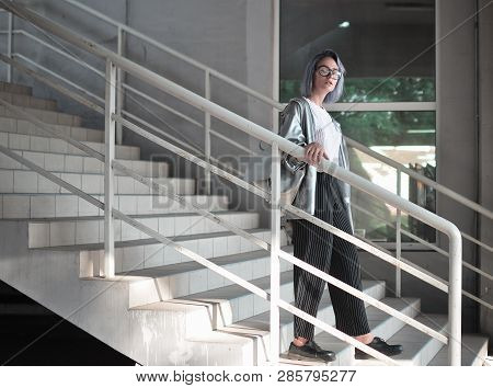 Atypical Beauty, An Attractive Girl In A Raincoat Of Silvery Fabric Goes Down The Stairs.