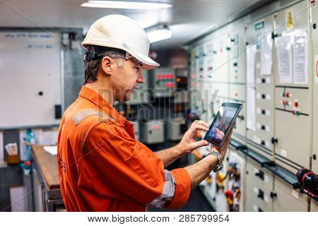 Marine Chief Engineer Watching Digital Tablet In Engine Control Room