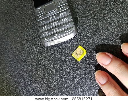 Female Fingers Reach For Sim Card Laying On Black Table Near Old Cellphone