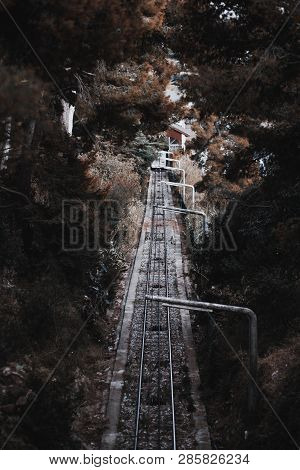 A Dark Atmospheric Railroad Track In A Corridor Of Greenery With A Small Depot Building In The End; 
