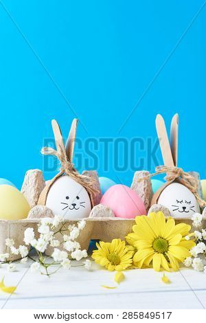 Easter Colored Eggs In Paper Tray With Decorationd On Blue Background