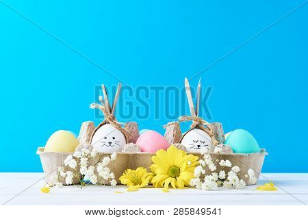 Easter Colored Eggs In Paper Tray With Decorationd On Blue Background
