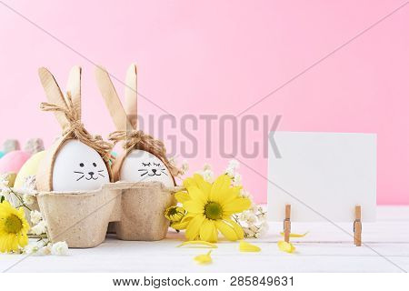 Easter Colored Eggs With Painted Faces In Paper Tray With Decorationd On Pink Background