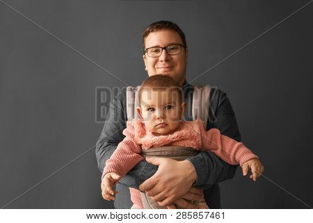 Fathre And His Kid In Baby Carrier At The Grey Background Wall, Baby Wearing Concept