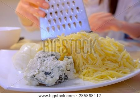 Woman Puts Rub Cheese On Grater On Plate With Different Sort Of Cheese. Hands Close-up.