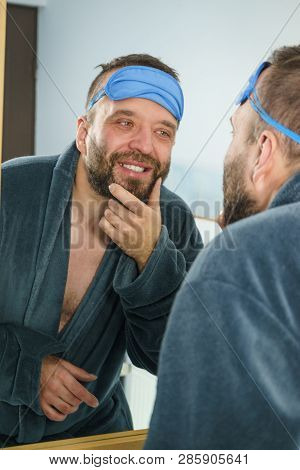 Adult Man With Eyemask On His Forehead Feeling Fresh After Waking Up, Looking At Himself In Bathroom