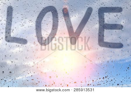 Inscription Love, On The Misted Glass. Glass Window With Raindrops Against The Sky. Concept Of Love 