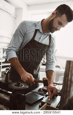 Traditional Tools. Male Goldsmith Wearing Apron Making A New Product At A Workbench Using Hammer