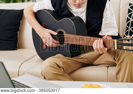 Cropped Image Of Serious Teenge Boy Enjoying Playing Guitar In Front Of Laptop When Streaming On His