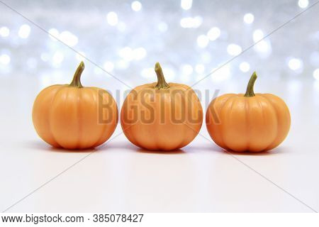 Three Small Orange Pumpkins On A Shiny Bokeh Background. Concept Of Autumn Decor, Halloween, Autumn 