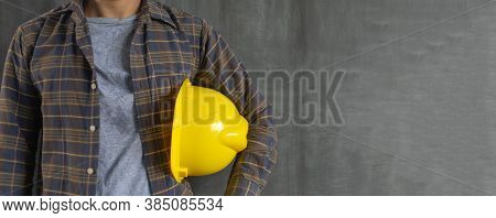 Construction Worker Holding Safety Helmet Yellow On Cement Wall Background With Copy Space