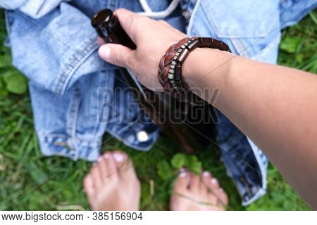 A Hand Of A Hippie, Hipster Holding A Bottle Of Alcohol, Beer. Young People With Alcohol Addiction C