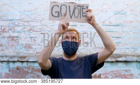 Man Shows Cardboard With Go Vote Sign On Brick Wall Urban Background. Voting Concept. Make The Polit