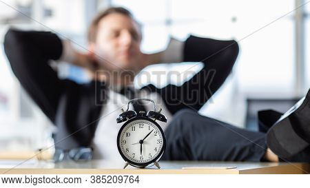 The Clock Shows Time After Office Hours Work On A Desk With A Businessman Sitting In A Blur Backgrou