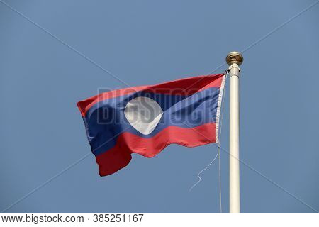 National Flag Of Laos On Bright Blue Sky Background. Blown Away By Wind. Laos Is One Of The Ten Asso