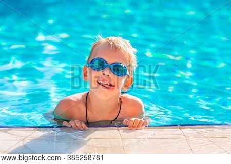 Cute Happy Little Boy In Goggles Swimming In The Swimming Pool