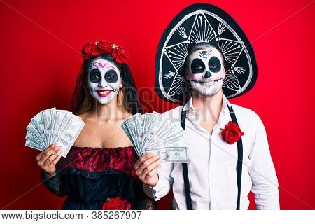 Couple wearing day of the dead costume holding dollars looking positive and happy standing and smiling with a confident smile showing teeth 