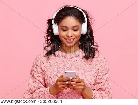 Delighted Young Ethnic Female Smiling And Browsing Social Media On Smartphone While Listening To Mus