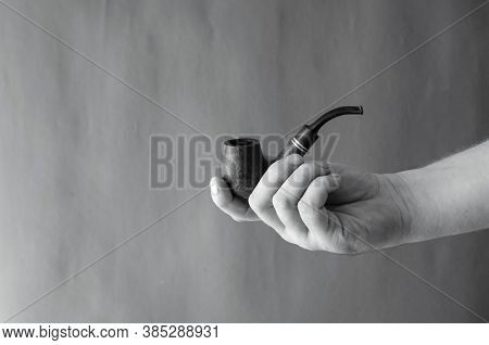 Smoking Pipe In Hand Against The Background Of A Textured Wall. An Adult Male's Right Hand Holds A S