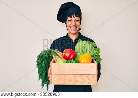 Beautiful brunettte woman chef holding fresh veggetables celebrating crazy and amazed for success with open eyes screaming excited. 