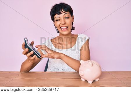 Beautiful brunettte woman caculating money savings winking looking at the camera with sexy expression, cheerful and happy face. 