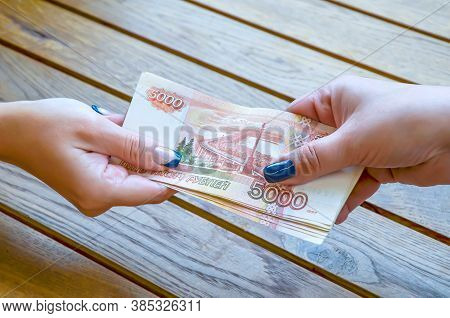 Two Female Hands Pass The Tutu Of Five-thousandths Russian Ruble Bill On The Background Of A Wooden 
