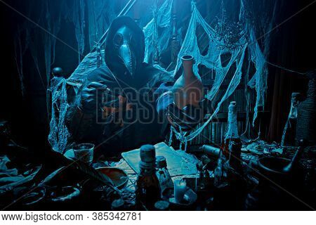 The plague doctor is working at his desk, inventing a cure for bubonic plague. The atmosphere of mysticism. Historical reenactment. Halloween. 