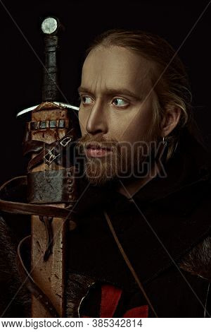 Portrait of a medieval knight in armour and with a sword over black background. Knight Templar. Historical reenactment.