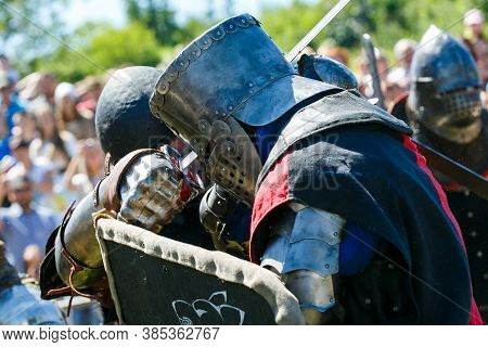 Knight Tournament. Medieval Restorers Fight With Swords In Armor At A Knightly Tournament