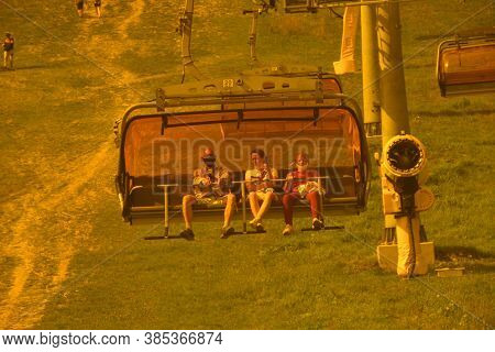 Hikers In Protective Masks On Their Faces Sit In A Cable Car To The Mountains