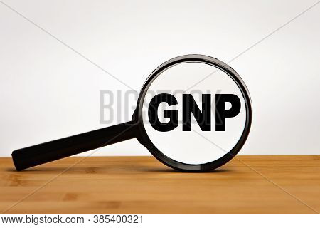 Focused On Business Concept. Magnifier Glass With Word Gnp Gross National Product On Wooden Table. B