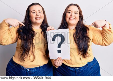 Young plus size twins holding question mark pointing finger to one self smiling happy and proud 