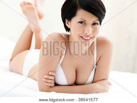 Kvinde i undertøj liggende i sengen med hvidt sengelinned, hvid baggrund