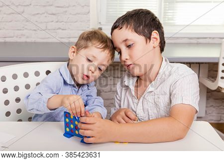 Two Funny Brothers Are Laughing And Playing A Board Game Together On The Desk At Home. Happy Childre