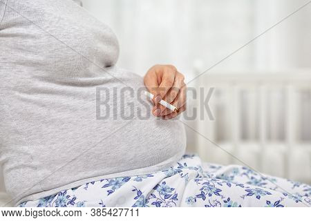 A Pregnant Woman With A Cigarette In Her Hands. Hand And Belly Close-up. The Concept Of Nicotine Add