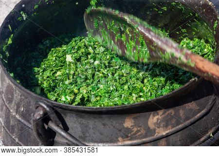 African cooking outdoors , spinach in a cast iron pot with a wooden spoon