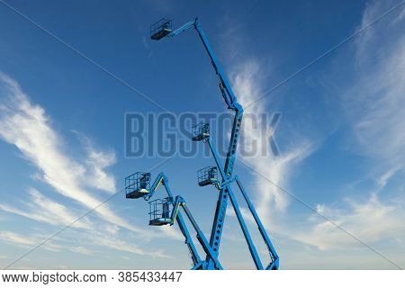 several blue hydraulic crane cherry picker against the sky