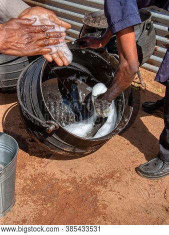 African man cleaning the pots in the yard, village in Botswana