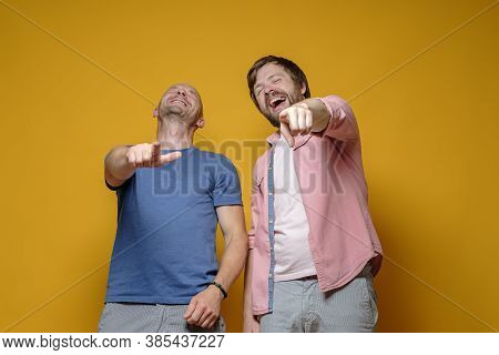 Two Caucasian Men In Casual Clothes Laugh Mercilessly At Someone And Point With Their Index Finger. 