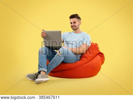 Young Man With Laptop On Bean Bag Chair, Yellow Background