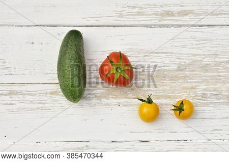 Red Tomato, Two Yellow Small Tomatoes And A Cucumber On A Wooden Vintage Table, Top View