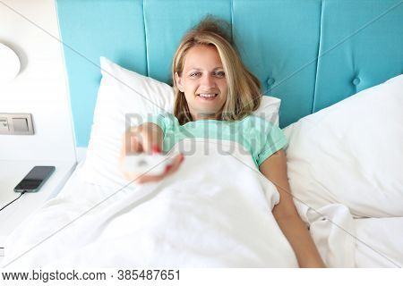 Young Woman In Bed Of Hotel Room Holds Remote Control In Hand. Remote Control Of The Quality Of Clim