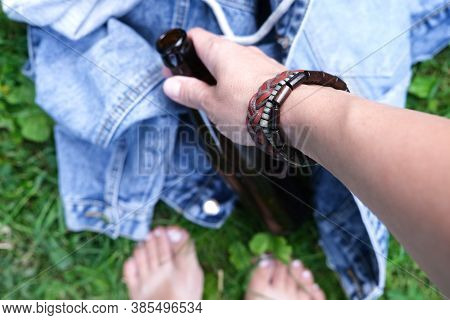 A Hand Of A Hippie, Hipster Holding A Bottle Of Alcohol, Beer. Young People With Alcohol Addiction C